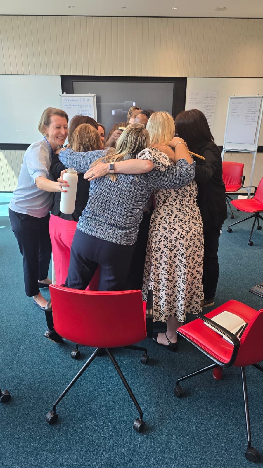 Participants at a Women2Lead cohort 2 workshop standing in a close group huddle, arms around one another
